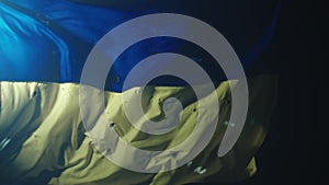 The developing blue yellow flag of Ukraine on a black background illuminated by a spotlight. Flag of Ukraine covered