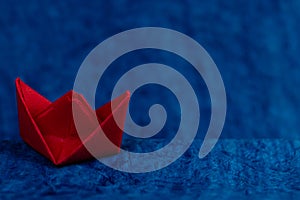 A deviating red paper boat down the high tide in ocean made with blue paper