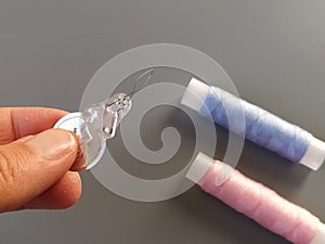 Device for drawing the thread into the eye of the needle. Bobbins with blue and pink threads in the background. A woman holds a