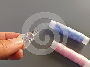 Device for drawing the thread into the eye of the needle. Bobbins with blue and pink threads in the background. A woman holds a