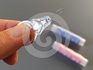 Device for drawing the thread into the eye of the needle. Bobbins with blue and pink threads in the background. A woman holds a