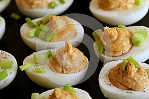 Deviled eggs with cod livers with leek on on black background