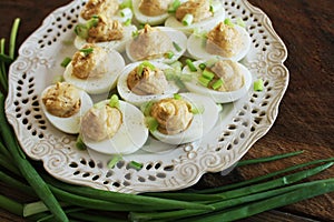 Deviled eggs with cod livers with leek on white plate. Rustic wooden table