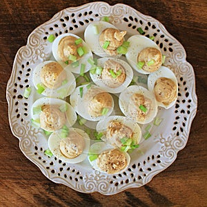 Deviled eggs with cod livers with leek on white plate. Rustic wooden table