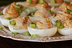 Deviled eggs with cod livers with leek on white plate. Rustic wooden table