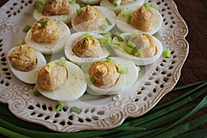 Deviled eggs with cod livers with leek on white plate. Rustic wooden table. Top view