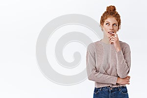 Devious, creative and pensive cute redhead woman with curly hair combed in bun, biting finger and looking up thoughtful