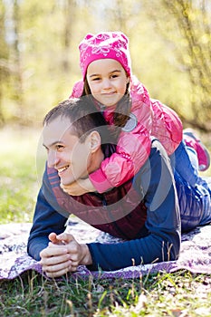 Devoted father and daughter lying on grass, enjoying each others company, bonding, playing, having fun in nature on a bright,