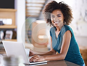 Devoted to success. Portrait of an attractive young woman smiling at camera while working on her laptop.