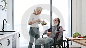 Devoted woman feeds man in wheelchair with fresh healthy salad.