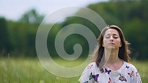 Devoted young woman sits with eyes closed and meditates outdoors, feeling wind