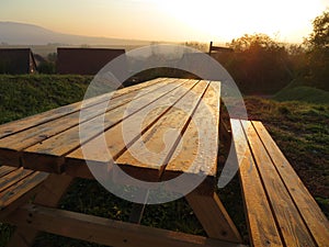 Dew-bespangled, wooden table and seats outdoor in sunrise.