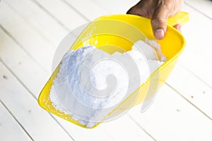 Dextrose in yellow shovel in hand on wooden white table.