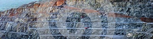 Diabase quarry stepped wall with two red drilling machines, panorama showing different layers of stone