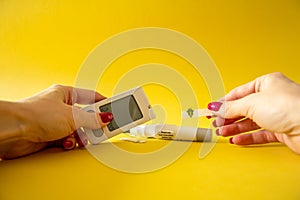 Diabet. Medical equipment. Medical concept. Close up of woman hands on yellow background using lancet on finger to check blood photo