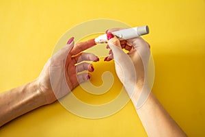 Diabet. Medical equipment. Medical concept. Close up of woman hands on yellow background using lancet on finger to check blood