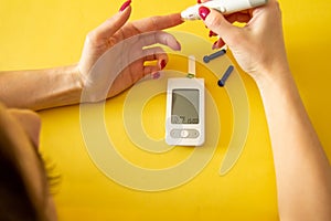 Diabet. Medical equipment. Medical concept. Close up of woman hands on yellow background using lancet on finger to check blood