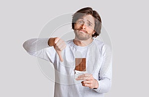 Diabetes and food allergies. Sad man shows thumb down and holds chocolate