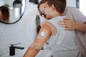 The diabetic boy brushing his teeth in the morning, preparing for the day, while wearing a continuous glucose monitoring