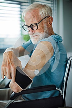 Diabetic senior man checking blood glucose level at home using continuous glucose monitor. Connecting CGM with