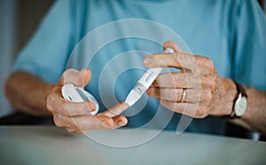 Diabetic senior man on wheelchair checking blood sugar level with fingerstick testing glucose meter.