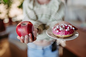 Diabetic woman is choosing between fresh apple and a sweet doughnut. Importance of proper nutrition and diet in diabetes