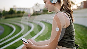 Diabetic woman sitting outdoors, watching social media content on smart phone.