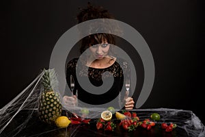 The diabolical young girl sitting at a table with fruits covered with spider web