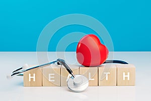 Diagnosis cardiologist concept. Text health on wooden cube blocks with red heart and stethoscope on blue background. Equipment