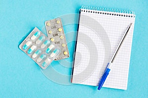 Diagnosis of the disease. Notebook with pen and pills on a blue background