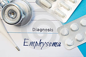 Diagnosis Emphysema. Doctor`s stethoscope, electronic thermometer and two blisters of pills lying near pad with inscription of dia