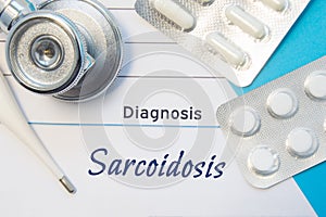 Diagnosis Sarcoidosis. Doctors stethoscope, electronic thermometer and two blisters of pills lying near pad with inscription of di