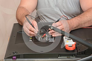 Diagnostics and repair of LCD TV. Engineer takes sample with multimeter on back of large monitor