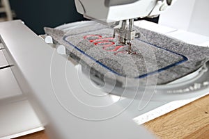 modern computerised sewing machine and embroidery unit with needle down stitching red lettering on grey felt in bright light