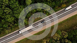 Diagonal drone or aerial view on tracks and driving cars on the road between trees. 4K resolution video. The drone