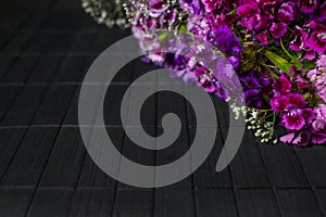 Diagonal frame of purple and violet flowers on dark wooden background, floral black background boards, copyspace
