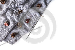 Diagonal grey knitting on needles with chestnuts, pine cones on a white background, place for text.