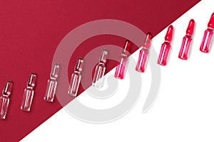 Diagonal line of ampules for injections with red and transparent liquid on isolated white and dark red background