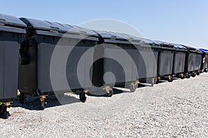 Diagonal row of black garbage containers on gravel outside