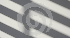 Diagonal shadows of blinds cast on a white wall create a pattern of parallel lines. The