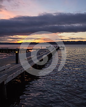 A diagonal view of a pier on a lake in a winter sunset at Waverly Beach Park, Washington, with Seattle skyline in the background