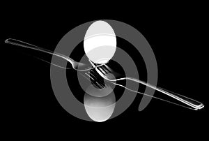 Diagonal view of white egg balanced on two forks with reflections on black background