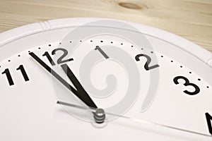 Dial of an analog clock close up on a wooden background. The time is 23:59. White dial, black numerals