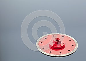 Diamond cutting wheel is red with a threaded nut on the mirror surface of a gray background with a slight gradient