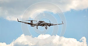 Twin engine piston aircraft during approach for landing on cloudy, sunny sky.