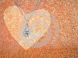 Diamond pendant and white gold necklace on an olded rose color heart carpet background. Use to with love in every festival.