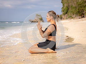 Diamond pose. Beautiful Caucasian woman sitting on the sand in Vajrasana. Hands in namaste mudra. Yoga and meditation concept.