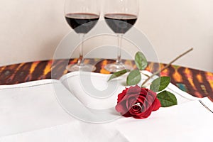 Diamond ring inside red rose over two wine glasses background