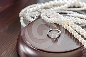 Diamond ring and perals on the wooden pad, on wooden table. Engagement/wedding ring.
