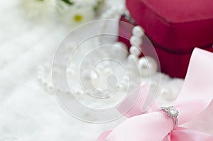 Diamond ring and pink ribbon on pearl necklace background